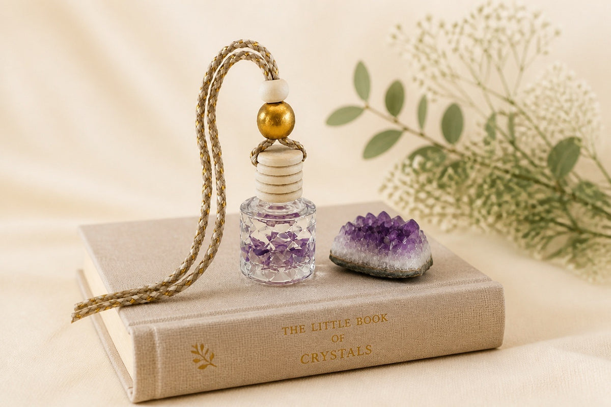 Crystal car diffuser with amethyst crystals beside an amethyst cluster, on a copy of The Little Book of Crystals